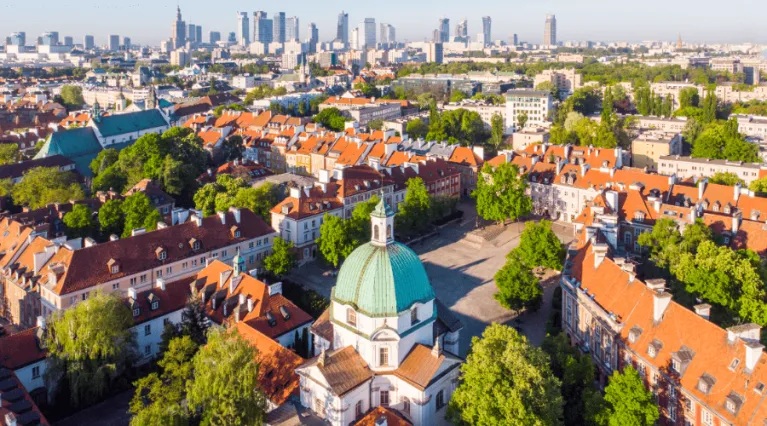 Widok z lotu ptaka na Starówkę warszawską. Dachy kamienic, drzewa i kopuła kościoła. 